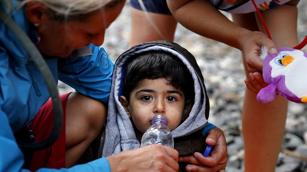 Una voluntaria ofrece agua a un niño sirio exhausto recién desembarcado en Lesbos.